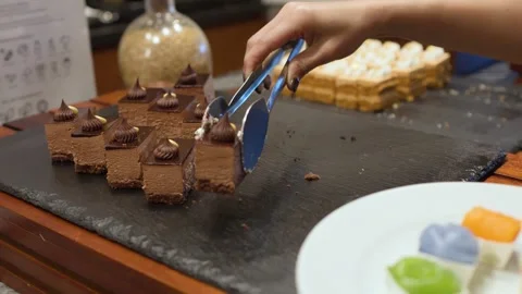 Hand Using Tongs to Pick Chocolate Mousse Cake from Buffet Platter 库存影片 333603449