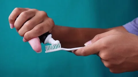 Hand using toothpaste onto brush isolated blue background 库存影片 275872436