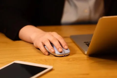 Hand using wireless mouse next to laptop on wooden desk Stock Photos