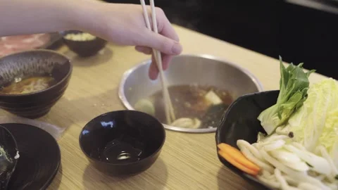 Hand using wooden chopsticks to pick up bok choy from a bowl of udon noodle.. Stock Footage 335707852