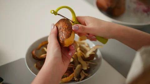 Hand view of person peeling potato over bowl filled with discarded potato skin Stock Footage 307952032