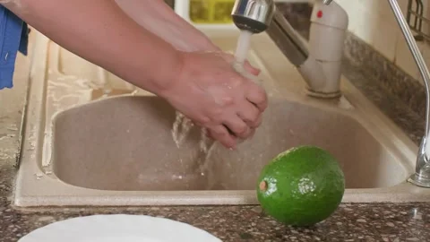 Hand washing avocado fruit under running water in kitchen sink Stock Footage 344728998