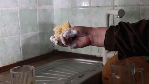 Hand washing kitchen tiles with a soapy sponge near the sink and faucet Stock Footage 339178886