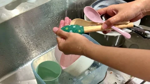 Hand washing a spoon under running water in a kitchen sink, highlighting Stock Footage 345289520