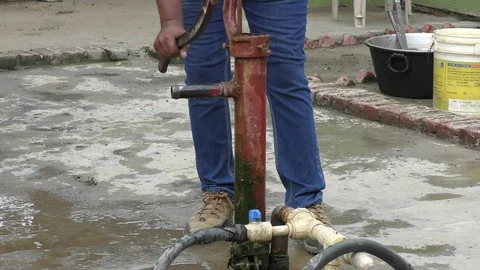 Hand water pump being used and pipe of red colors Stock Footage 114393245