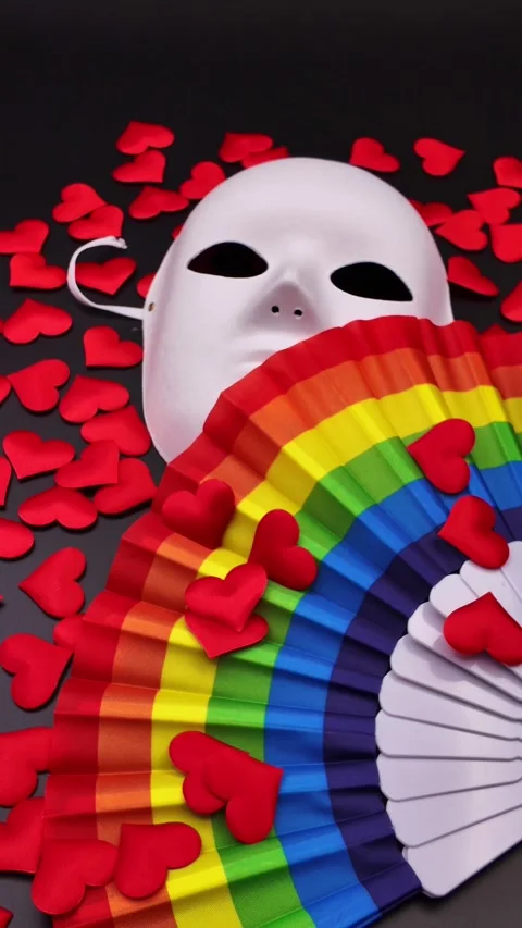Hand waving a rainbow fan in front of a white mask for LGBTQ pride Video stock 329451742