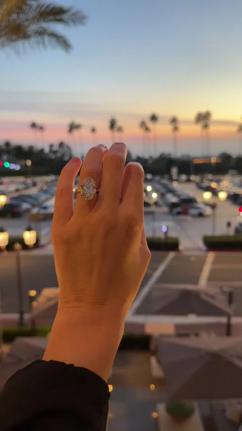 Hand wearing large oval diamond solitaire engagement ring with traffic at sunset Stock Footage 325876555