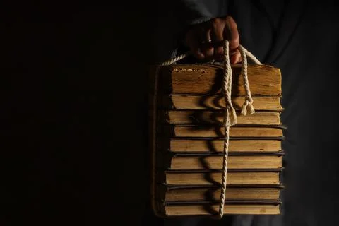 A hand will pull out of the darkness a stack of old books tied with rope Foto stock