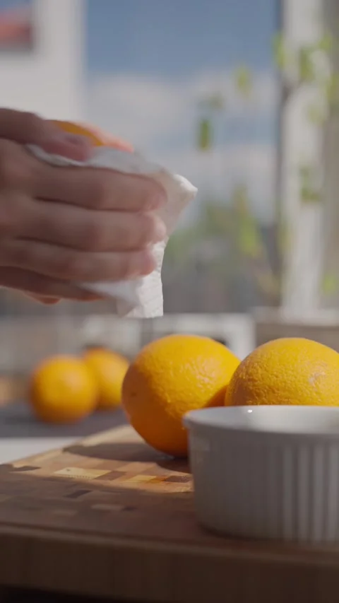 Hand wipes orange with paper towel on kitchen counter with fresh oranges nearby Stock Footage 337657841