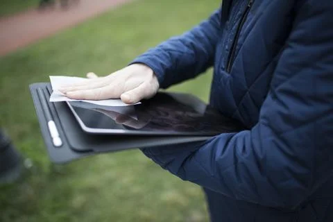 Hand wiping a tablet screen with a cloth outdoors in a park Stock Photos
