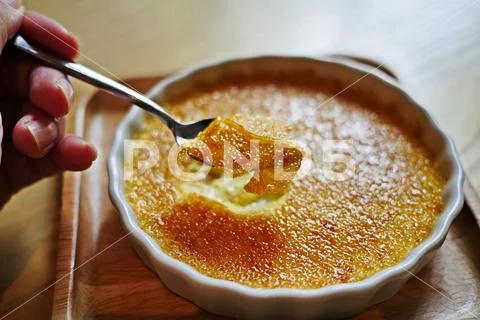 A hand of woman cracked through a crunchy top layer of a Creme brulee, burnt Stock Photos