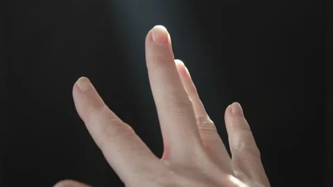 The hand of a woman on a dark background in the rays of the bright sun moves her Stock Footage 233001380