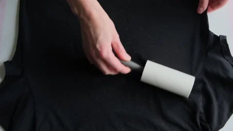 Hand of a woman using lint roller to clean black t-shirt. Stock Footage 329768236