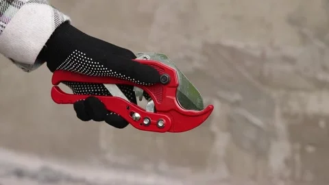 A hand in a work glove holds a red pipe cutter for plastic pipes Stock Footage 336620967