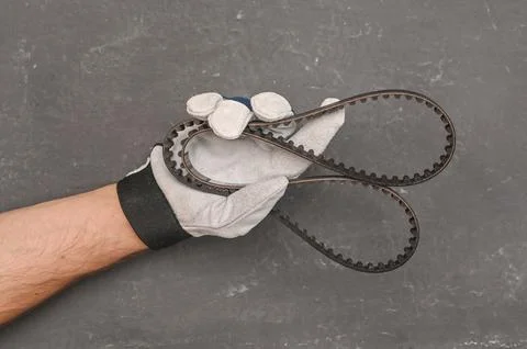 Hand in a work protective glove of auto technician holding rubber belt in w.. Stock Photos