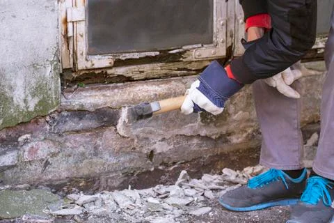 Hand of worker with gloves hammering down plaster on facade that crumbles Stock Photos