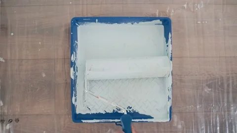 Hand in working glove dips paint roller into the yellow tray with grey paint Stock Footage 152908254