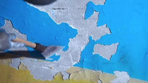 Hand in a working glove using a metal scraper to remove layers of old blue pa Stock Footage 333532072