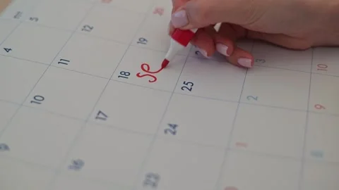 A hand writes on a calendar using a red marker, marking specific dates. The red Stock Footage 337556427