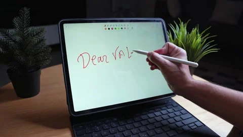 Hand writes Dear Valentine message on tablet with stylus at desk, indoor Stock Footage 328615566