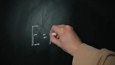 A hand writes the famous equation Emc squared on a blackboard. The action Stock Footage 338186442