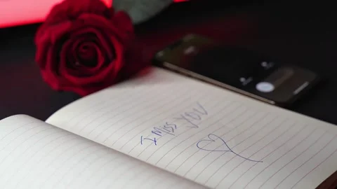 Hand writes I miss you message in notebook with rose and phone, close-up Stock Footage 328491277