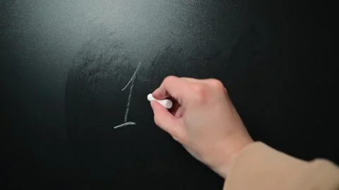 A hand writes a math equation on a blackboard using chalk. The action takes Stock-Footage 338186395