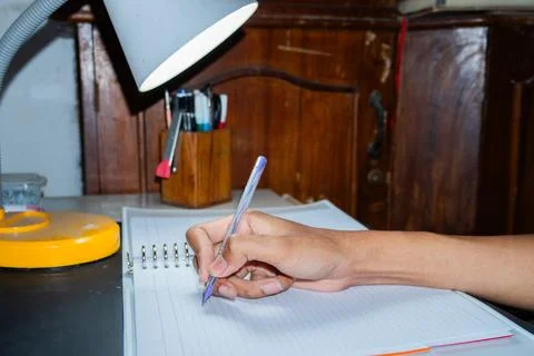 Hand writes in notebook under focused desk lamp Stock Photos
