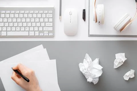 Hand writes notes on piece of paper in modern workspace. Crumpled pieces of Stock Photos