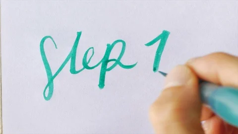 Hand writes STEP 1 in cursive with a green brush pen on white paper Stock Footage 93409030