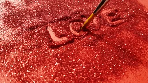 Hand writes text love on red sparkles with a brush Video stock 169414891