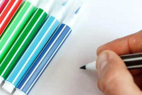 Hand writes on a white sheet next to lying colored markers Foto stock