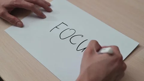 A hand writes the word focus on a sheet of paper. The writing style transitions Stockbeeldmateriaal 337550244