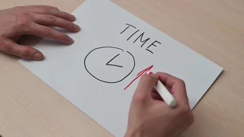 A hand writes the word time and draws a clock on a sheet of paper. The process Видео 337550452