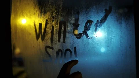 A hand writes the word winter, snow on a fogged window. it's snowing behind the Stock Footage 166463945