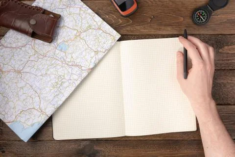 Hand writing in blank notepad with compass, knife, gps navigator and map on w Stock Photos