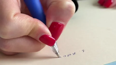 A hand is writing with a blue pen on a beige surface. 库存影片 340526569