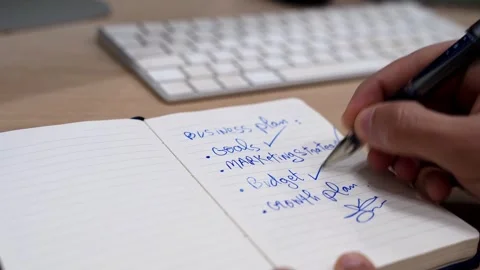 Hand Writing Business Plan Checklist in Notebook with Pen on Office Desk Close Stock Footage 332073347