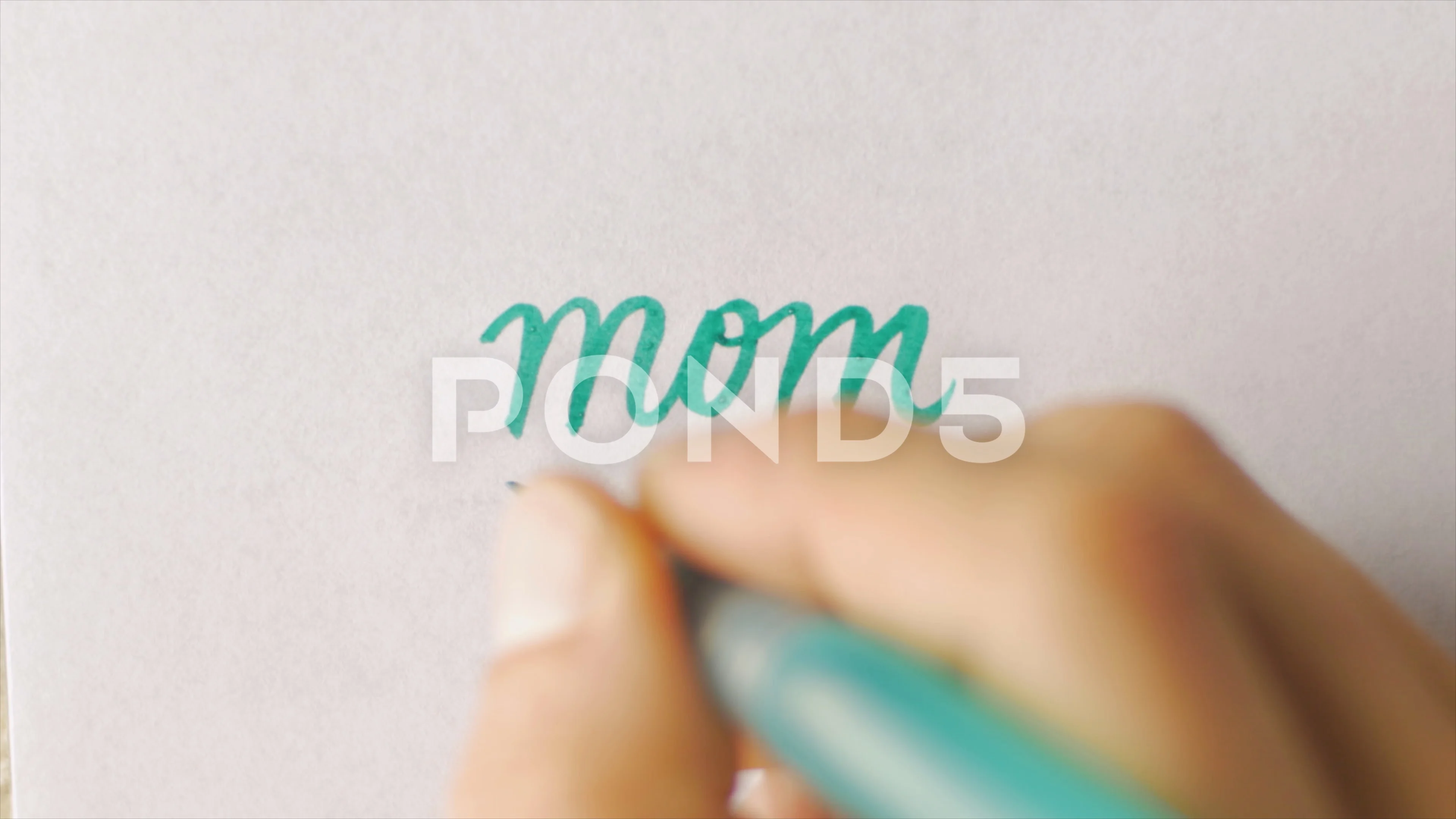 Hand writing MOM in cursive with a heart below the word