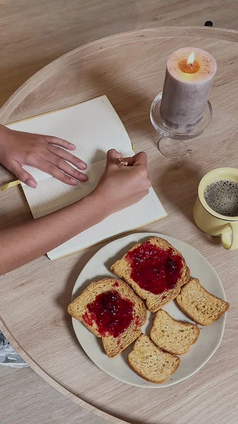 Hand writing in notebook beside breakfast toast and coffee Stock Footage 331773069