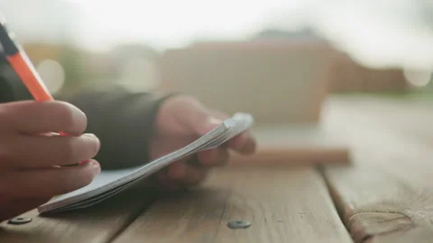 Hand Writing In Notebook On Wooden Table Outdoors With Open Book In Background Stock Footage 318852871