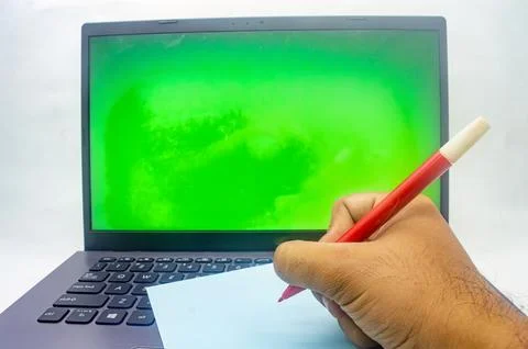 A hand writing on a notepad in front of a laptop with a green screen, isola.. Stock Photos