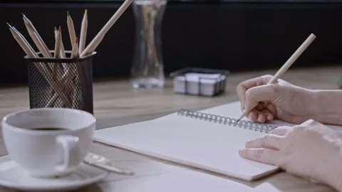 Hand writing the pencil to in book with table, view of room on the morning Stock Footage 105143396