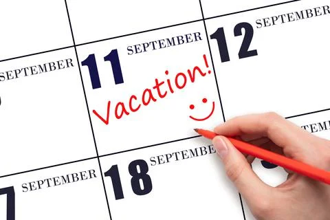 A hand writing a VACATION text and drawing a smiling face on a calendar date  Stock Photos