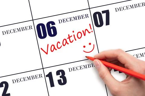 A hand writing a VACATION text and drawing a smiling face on a calendar date  Stock Photos