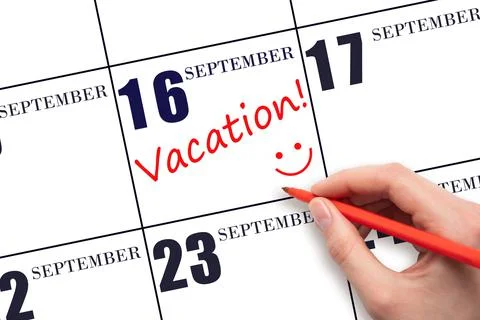 A hand writing a VACATION text and drawing a smiling face on a calendar date  Stock Photos