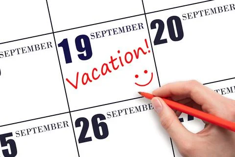 A hand writing a VACATION text and drawing a smiling face on a calendar date  Stock Photos