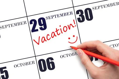 A hand writing a VACATION text and drawing a smiling face on a calendar date  Stock Photos
