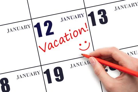 A hand writing a VACATION text and drawing a smiling face on a calendar date  Stock Photos