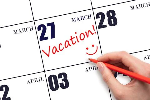 A hand writing a VACATION text and drawing a smiling face on a calendar date  Stock Photos
